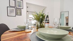 Une table à manger dressée avec des assiettes, des verres et une bouteille, entourée de tableaux encadrés accrochés au mur.