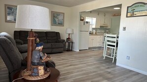 Un salon avec un canapé, une table en bois sur laquelle se trouve une lampe, et une cuisine à l’arrière-plan.