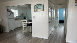 Une cuisine avec des meubles blancs, une table à manger avec des chaises et une pancarte sur laquelle on peut lire : « NOTRE MAISON DE VACANCES AU BORD DE LA MER ».