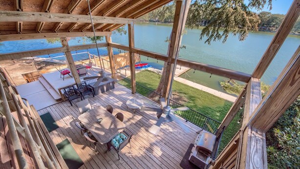 Una terraza de madera con mobiliario exterior, vistas a un lago y un barco.