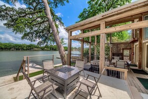 A wooden deck with a marble table and chairs overlooking a lake, connected to a building with a balcony and outdoor seating. - Ld 247 Waters Edge At Lake Dunlap 4 Bedroom Home by RedAwning (New Braunfels)