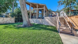 Una casa moderna con una terraza de madera, una escalera y un gran árbol en el jardín.
