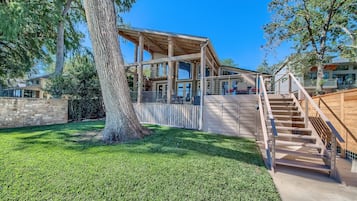 A modern house with a wooden deck, a staircase, and a large tree in the yard.