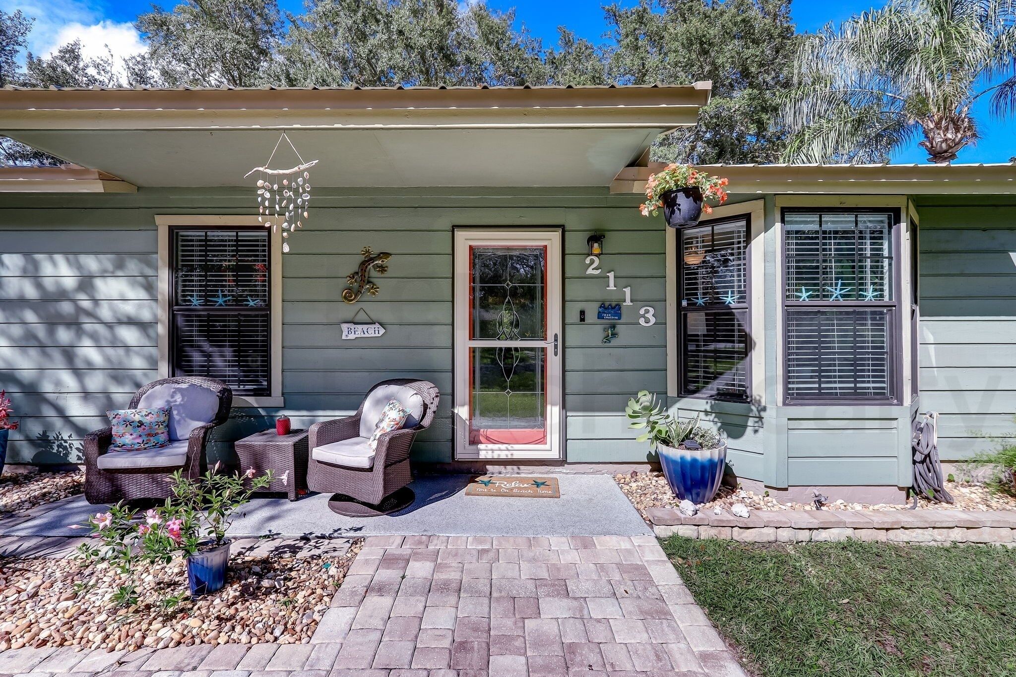 A house with a porch, two wicker chairs, a potted plant, and a 'Relax' sign.