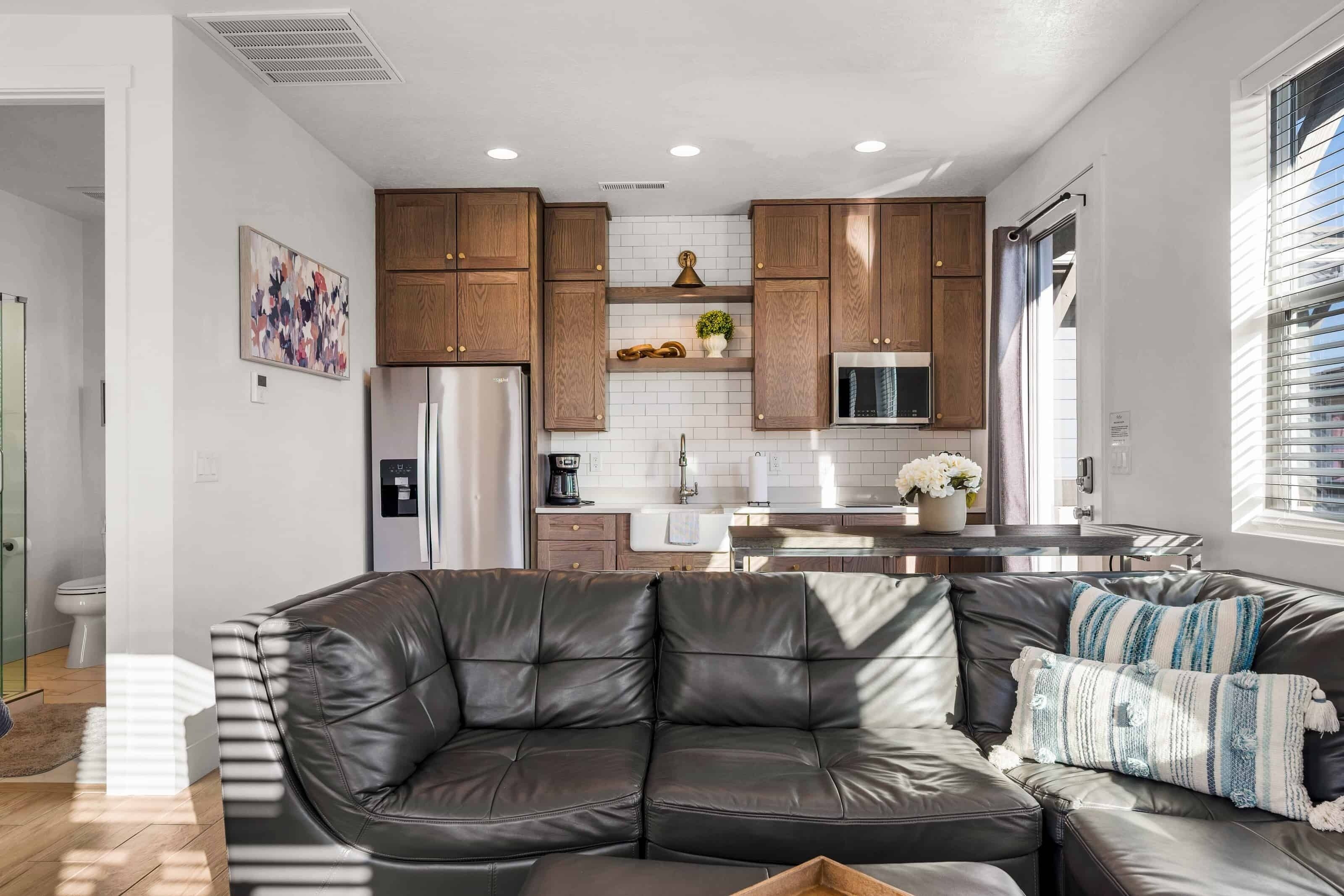 Una cocina moderna con armarios de madera, un refrigerador de acero inoxidable y un microondas. Hay un comedor con una mesa y sillas, y una sala de estar con un sofá de cuero y un cojín decorativo.