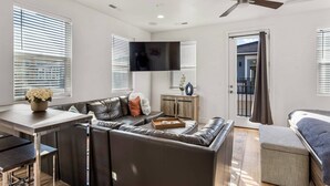 A modern living room with a sofa, a coffee table, a TV mounted on the wall, and a ceiling fan.