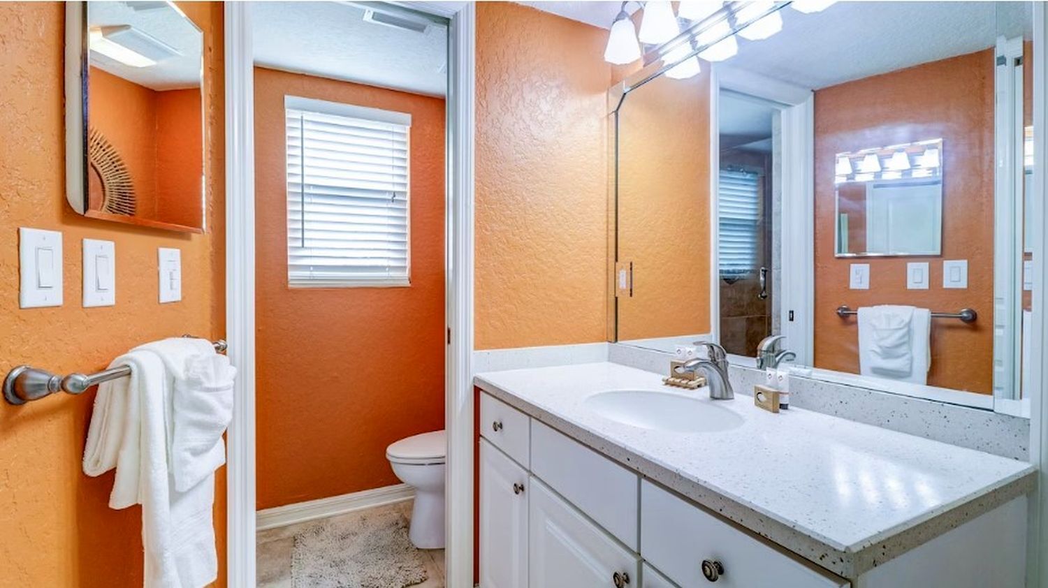 Un baño con una pared naranja, un lavabo blanco y un espejo grande.