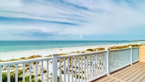 A beach view from a wooden deck with white railings.