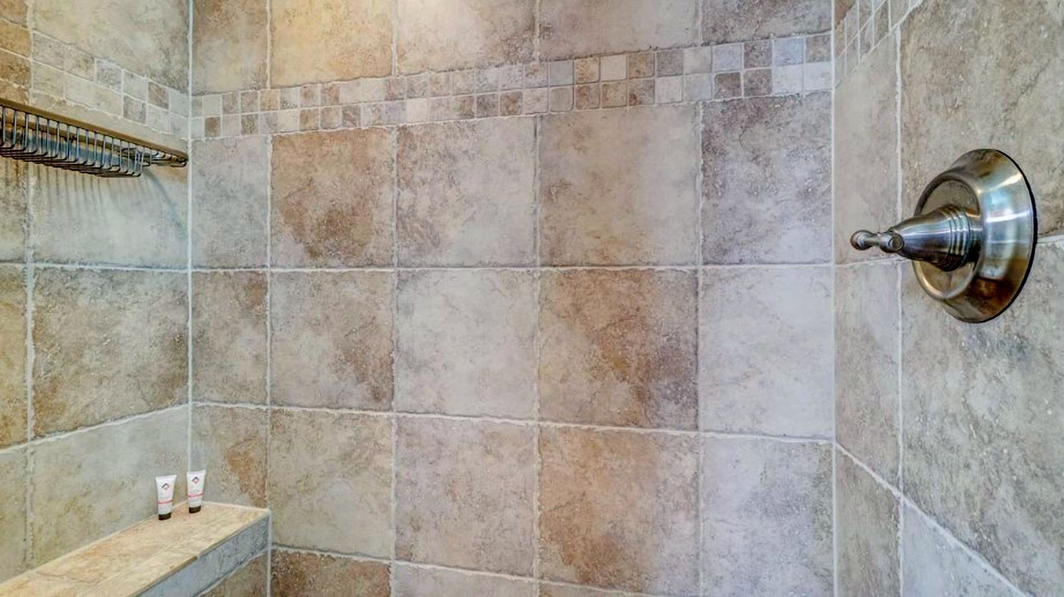 Un baño con baldosas de piedra, una cortina de ducha y un estante con artículos de aseo.
