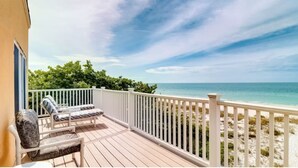 A wooden deck with white railings, a lounge chair, and a view of the ocean.