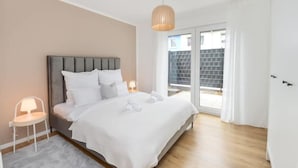 Une chambre à coucher moderne avec un grand lit, une table de chevet, une lampe et une vue sur l’extérieur.