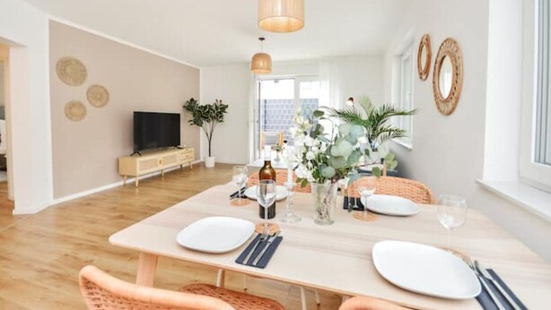 Un espace repas moderne avec une table en bois dressée pour quatre personnes, entourée de chaises en osier.