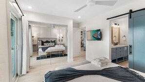 Een moderne slaapkamer met een groot bed, een plafondventilator, een schuifglazen deur naar een badkamer en een blauwe deur.