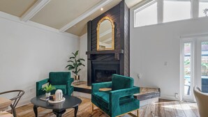 A living room with two green armchairs, a round coffee table, a fireplace with a mirror, and a potted plant.