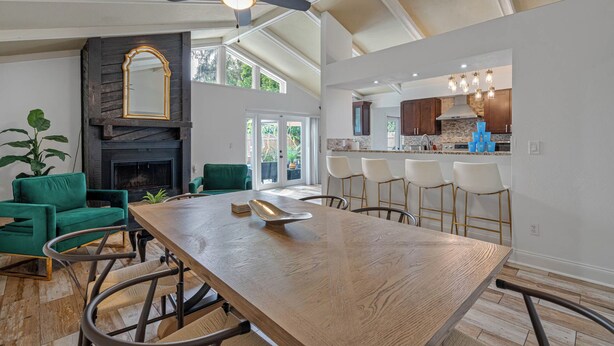 A spacious living room with a wooden dining table, green chairs, and a fireplace.