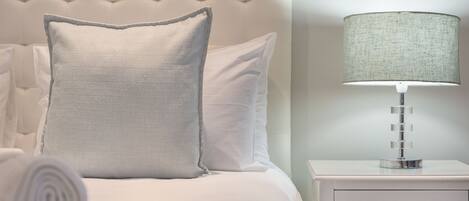 A neatly made bed with a pillow and a rolled towel, a bedside lamp, and a nightstand with a drawer.