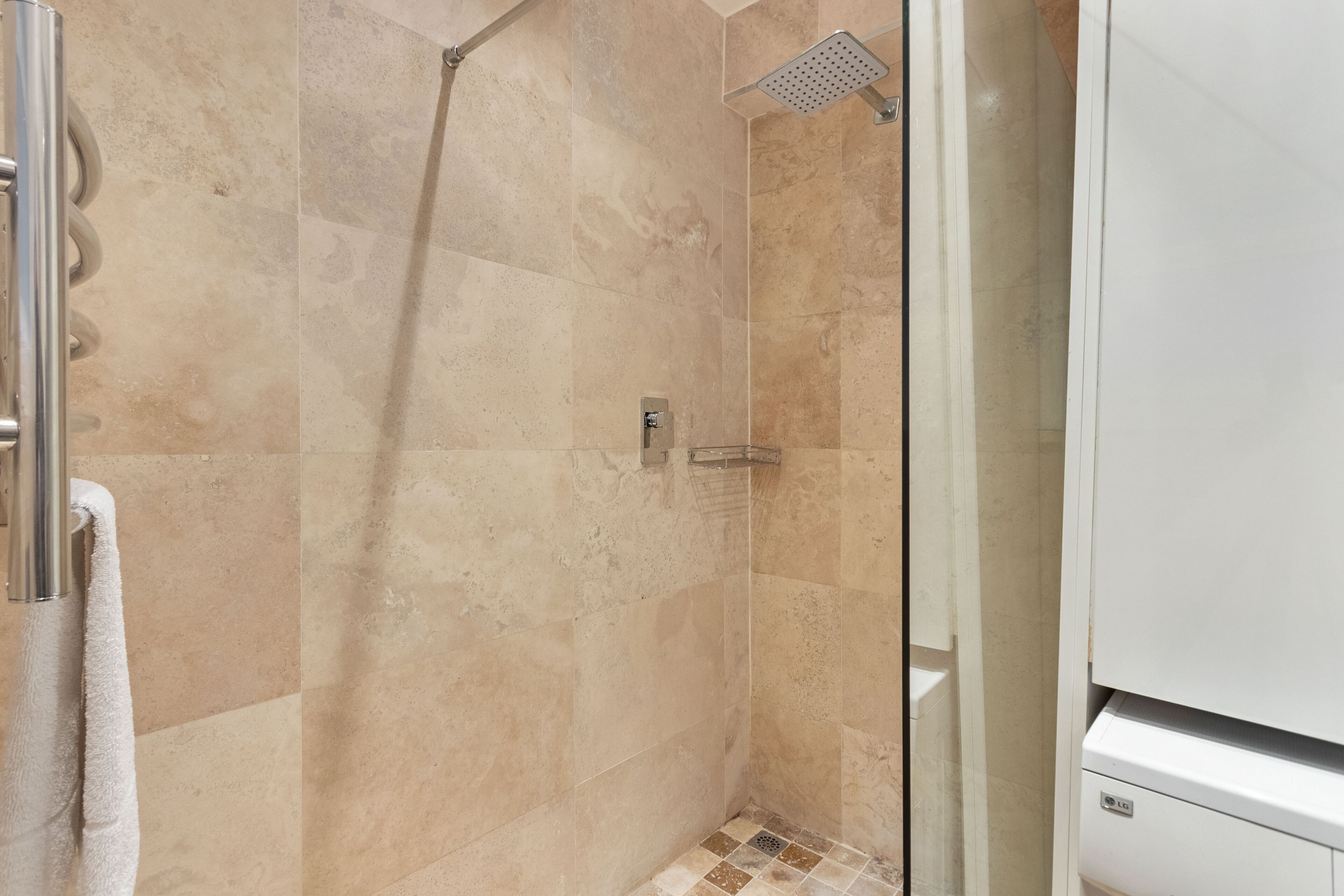 A shower with beige tiles, a glass door, and a towel hanging on a metal fixture.