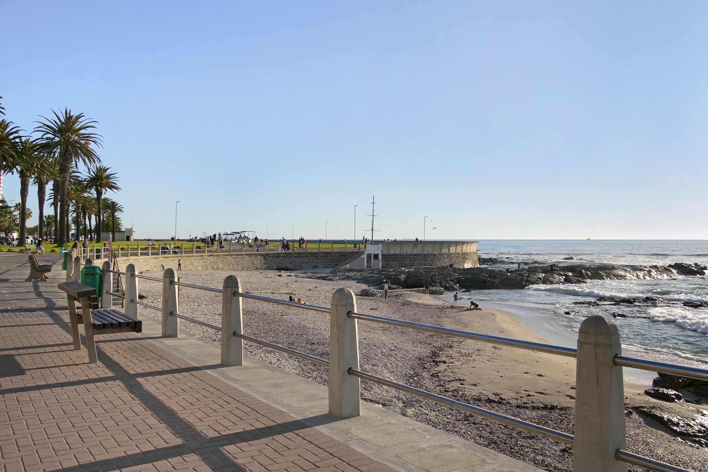 A coastal promenade with a paved walkway, benches, and a railing overlooking the beach.