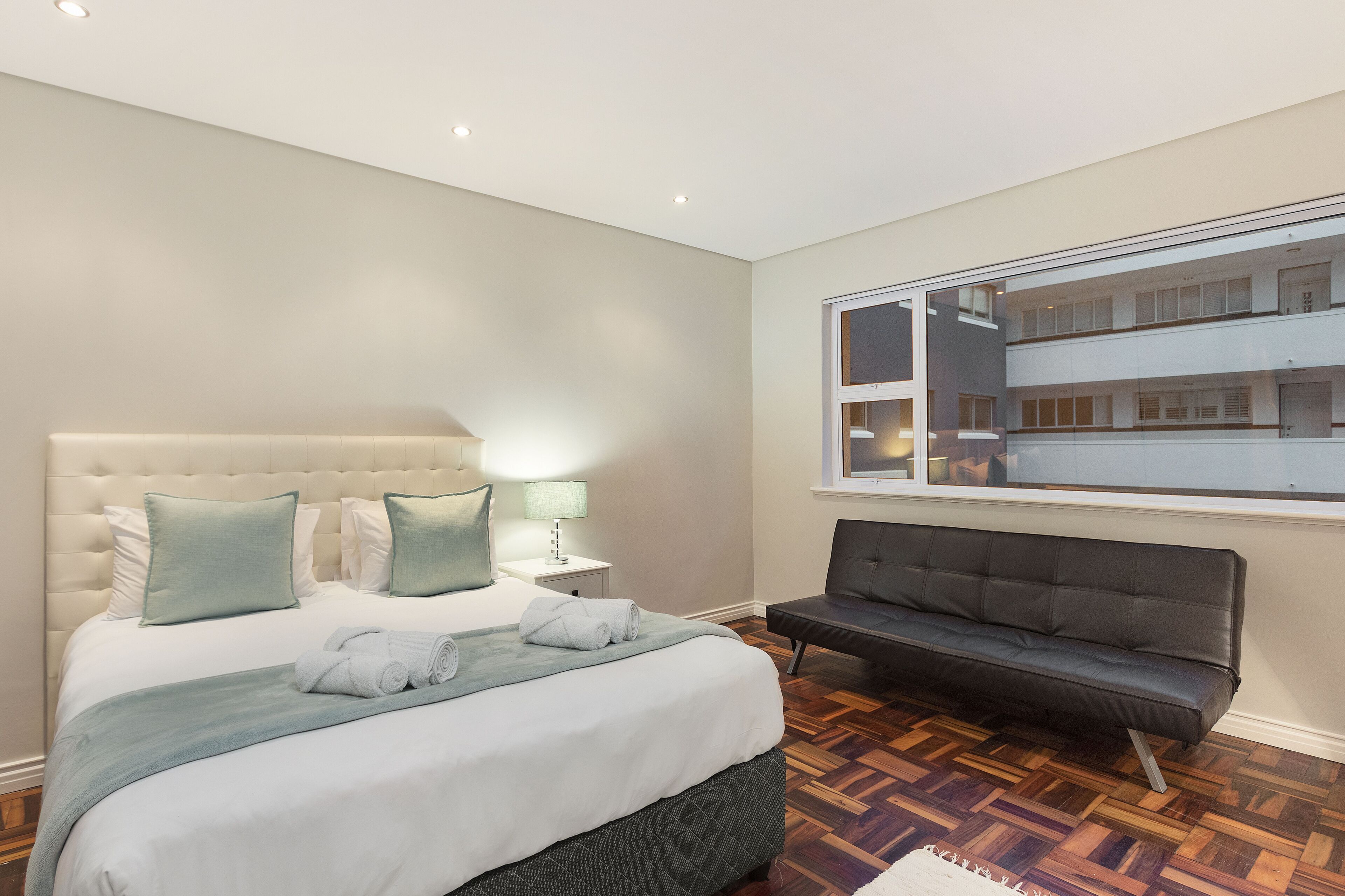 A bedroom with a large bed, a sofa, a window, and a view of a building.