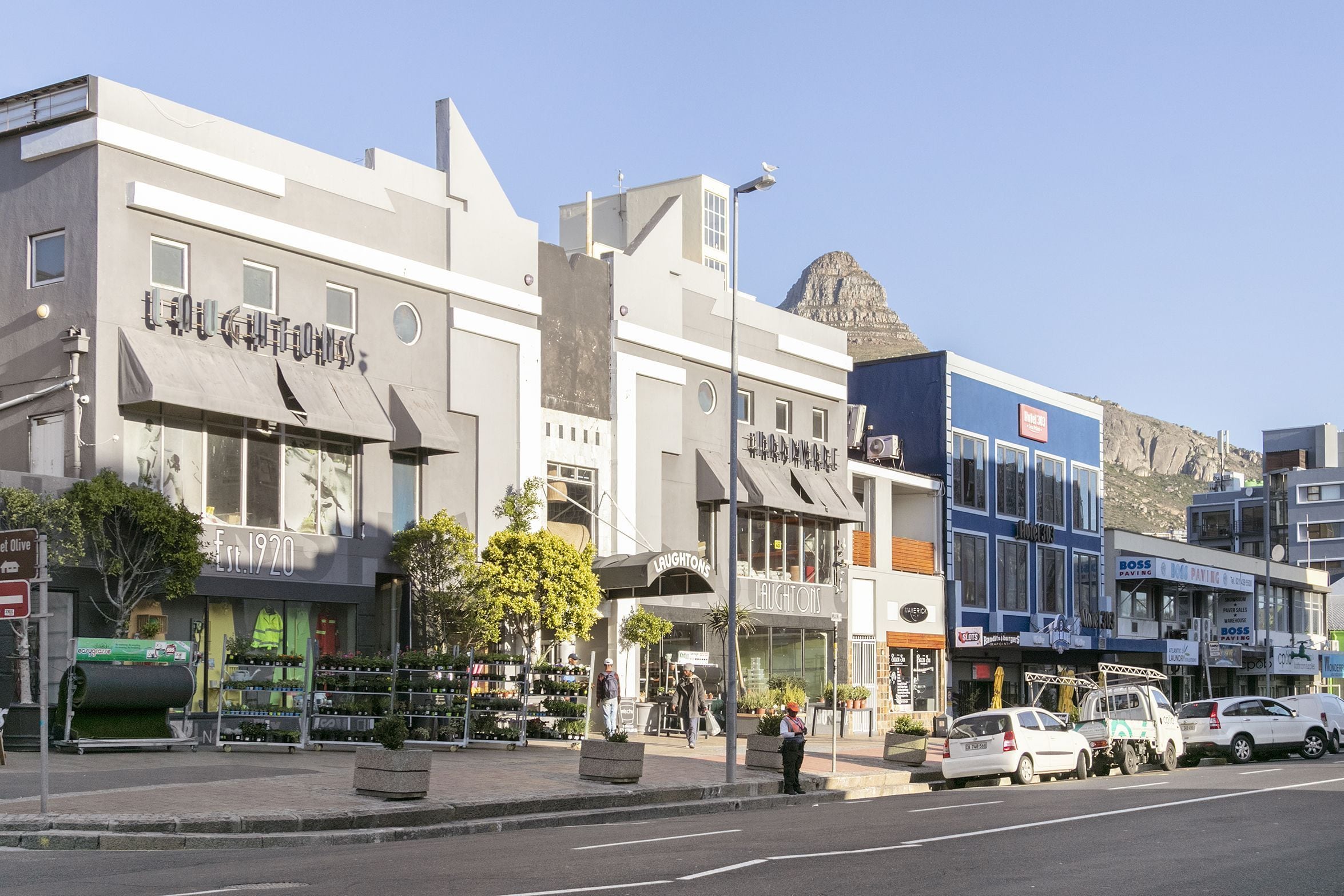 A street view with a building labeled 'Laughlins' and another with 'Boss'. There are cars parked along the street and a mountain in the background.
