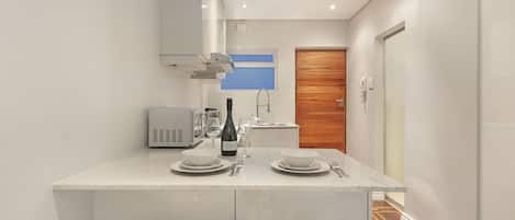 Un baño moderno con dos lavamanos blancos, una encimera con una botella de vino, vasos y un microondas.