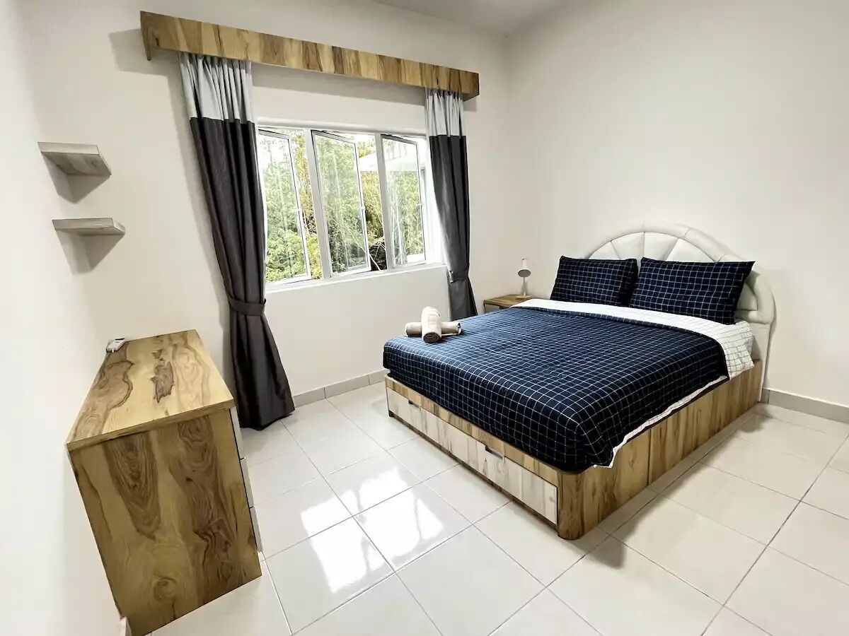 Ein Schlafzimmer mit einem Bett, einem Nachttisch aus Holz, einem Fenster mit Vorhängen und Blick ins Grüne.