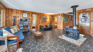 A cozy cabin interior with a stone-tiled floor, a blue sofa, a bookshelf, a fireplace, and wooden walls.