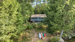 A cabin surrounded by dense forest, with a visible deck and a path leading to it.
