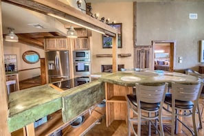 A kitchen with wooden cabinets, stainless steel appliances, and a round dining table with chairs. - LD 247 Waters Edge at Lake Dunlap (New Braunfels)