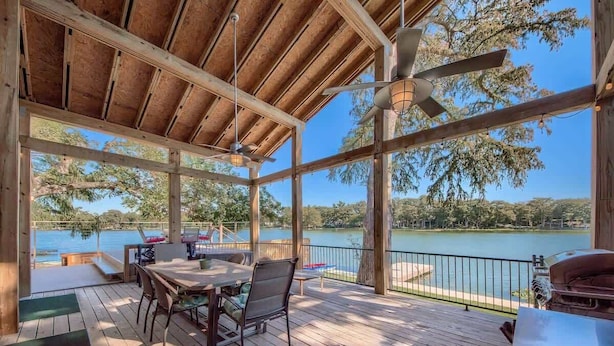 A covered outdoor area with a wooden deck, a table with chairs, and a view of a lake.