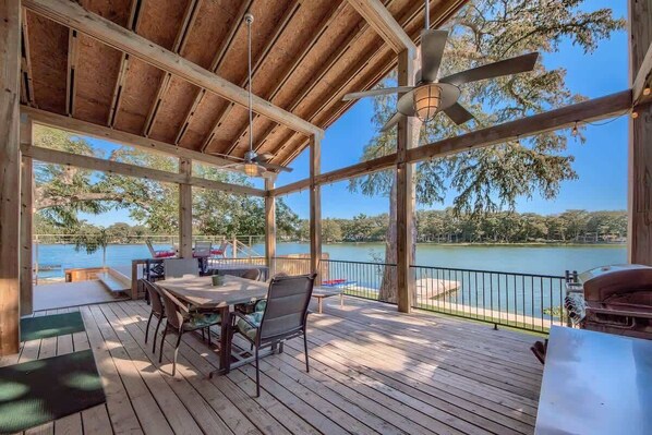 A covered outdoor area with a wooden deck, a table with chairs, and a view of a lake.