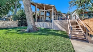 A wooden deck with a staircase leading to a covered area, surrounded by a well-maintained lawn and trees.
