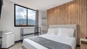 Quarto de hotel moderno com uma cama grande, vista da cidade pela janela e uma parede de destaque em madeira.