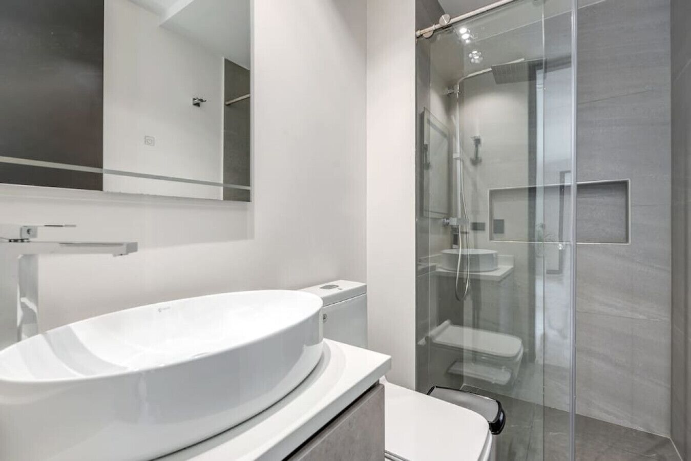 A modern bathroom with a large white sink, a glass shower enclosure, and a mirror above the sink.