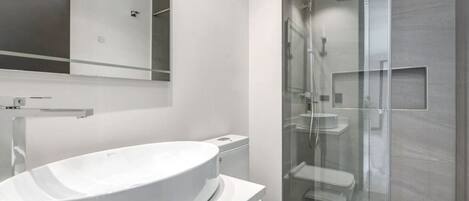 A modern bathroom with a large white sink, a glass shower enclosure, and a mirror above the sink.