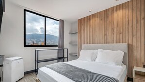 Une chambre d’hôtel moderne avec un grand lit, une vue sur la ville par la fenêtre, un mur d’accent en bois et une petite table de chevet.