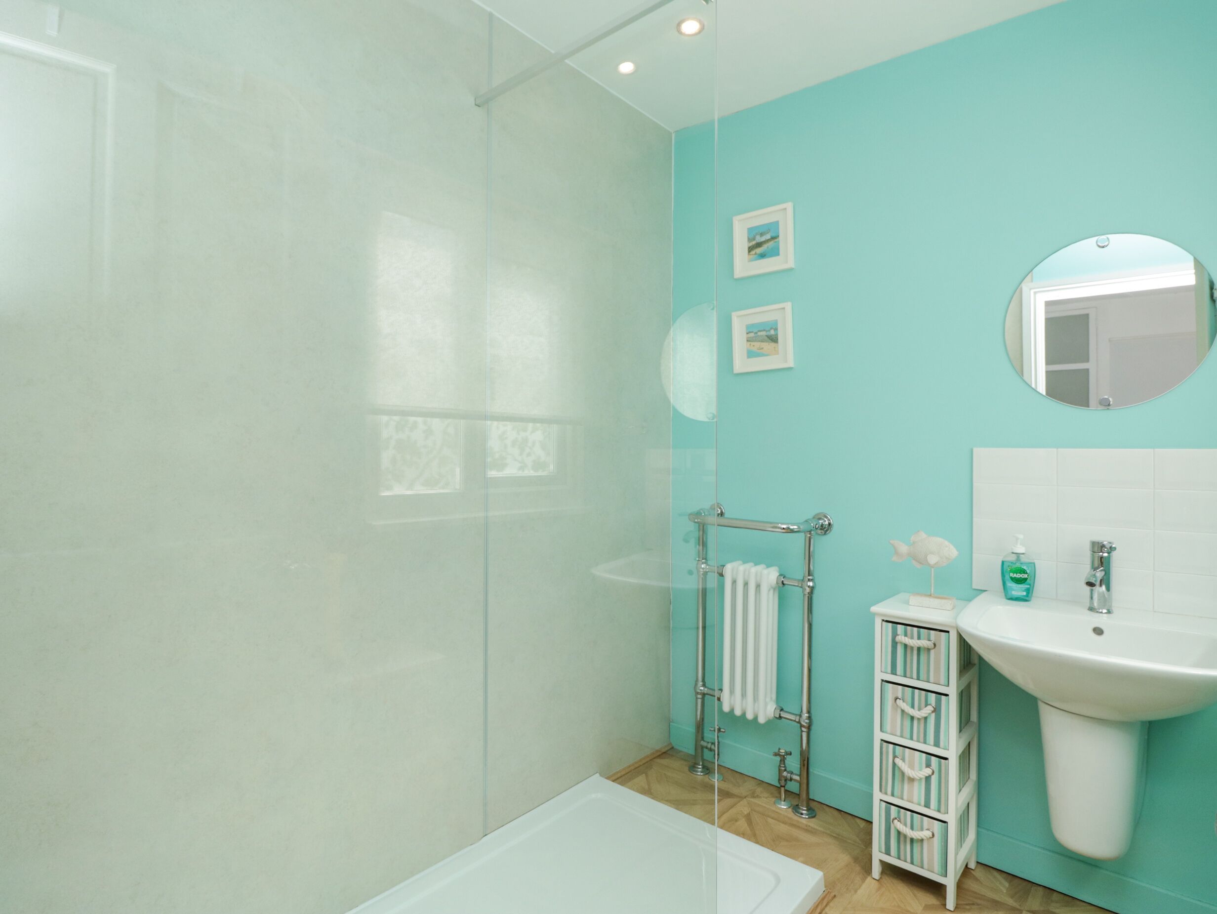 Une salle de bain avec une douche à parois de verre, une baignoire blanche, un lavabo avec un miroir et une petite étagère contenant des articles de toilette.