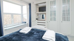 Un dormitorio con una cama grande, un armario, un televisor y una ventana con vista a la playa.