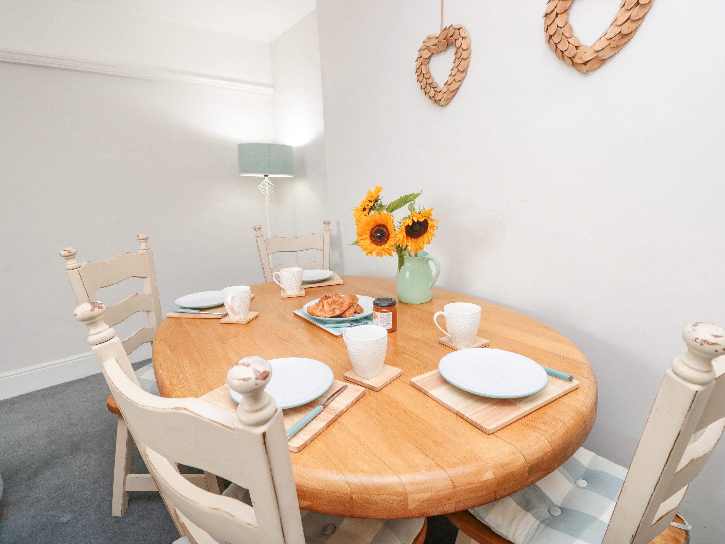 Ein runder Holztisch mit weißen Stühlen, eine Vase mit Sonnenblumen und eine Lampe in einer Ecke.