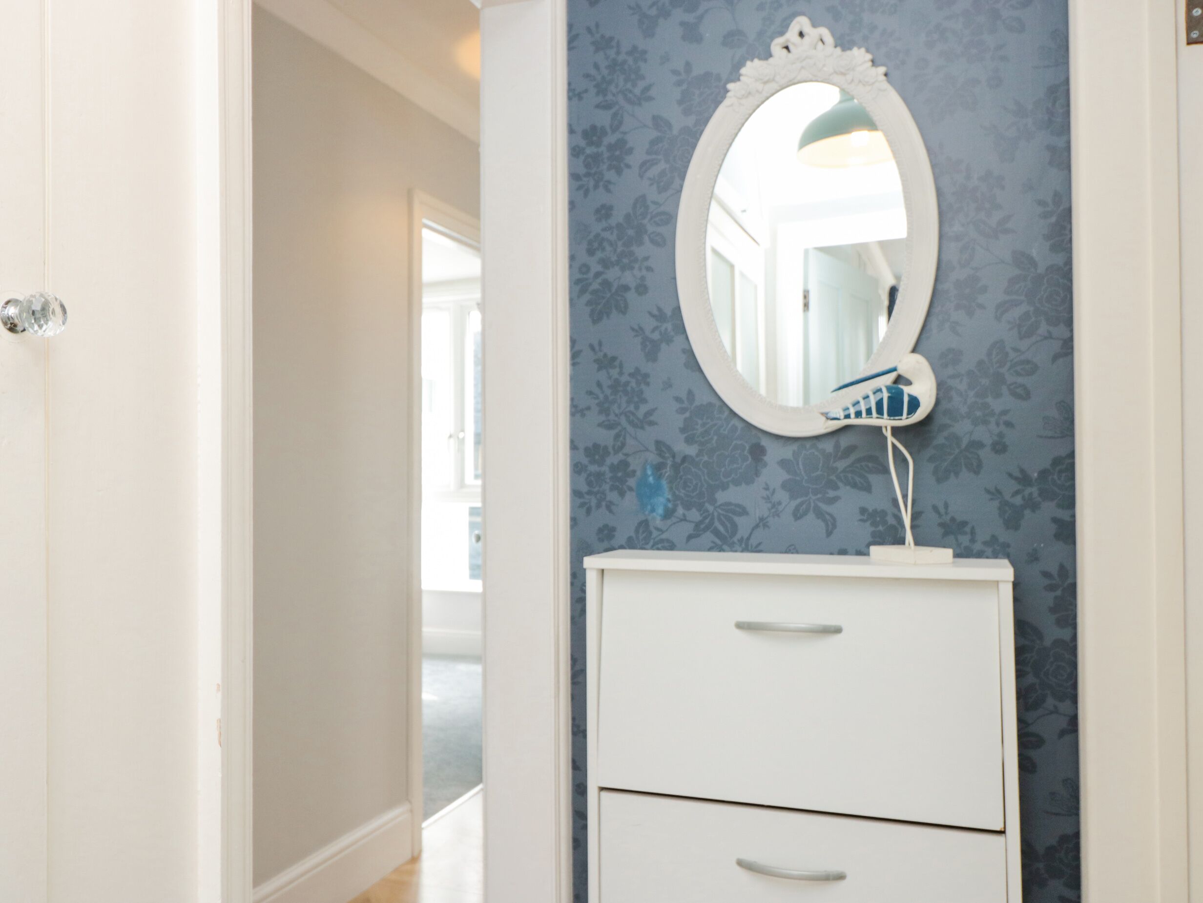 A bathroom with a white vanity, a mirror, and a floral-patterned wall.