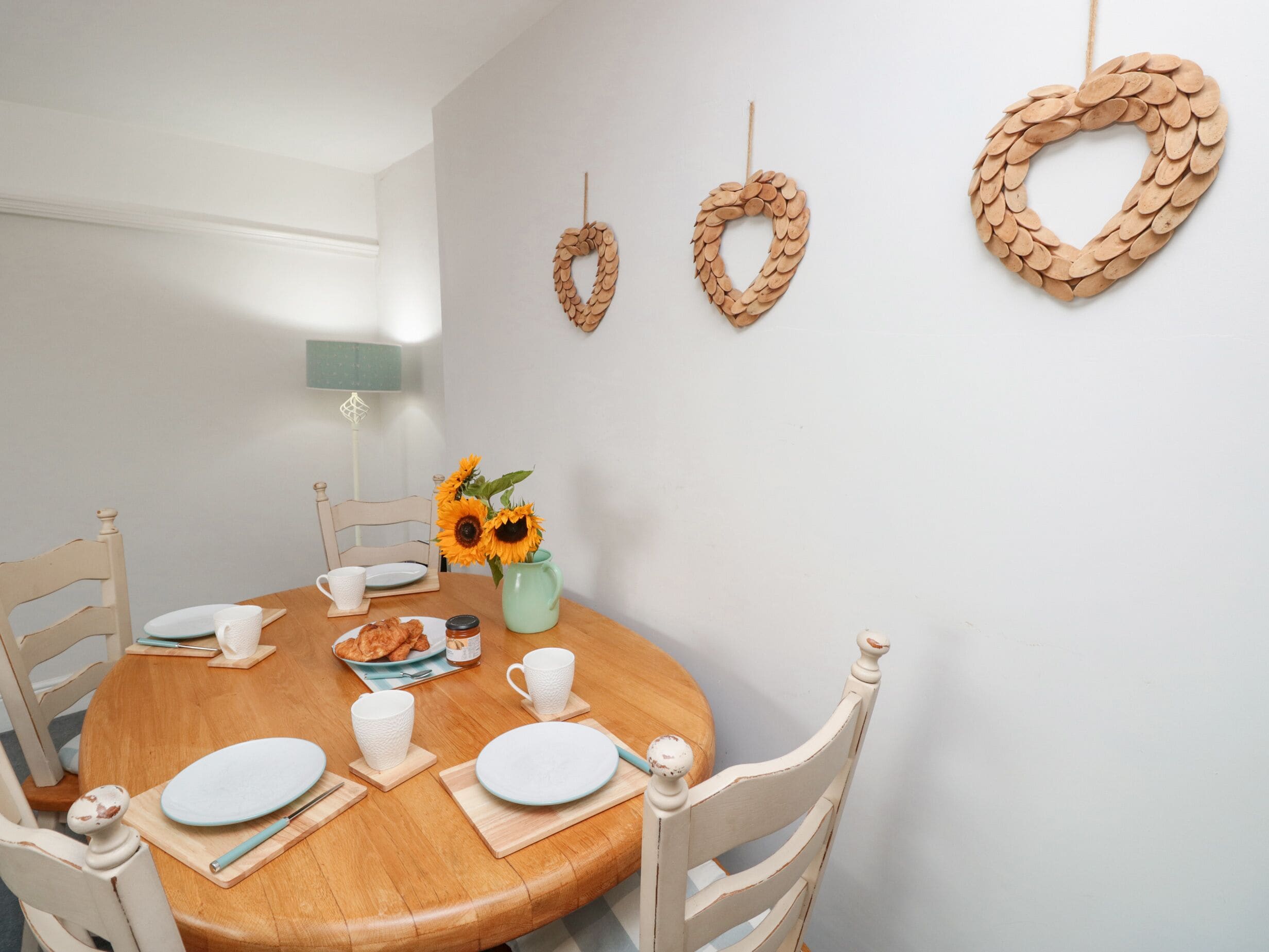 Un comedor con una mesa redonda de madera, sillas blancas y un jarrón con girasoles.