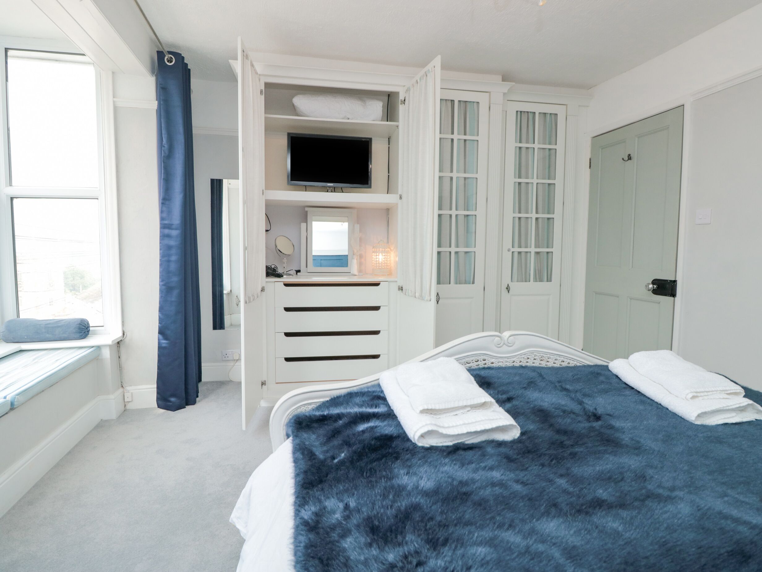 A bedroom with a bed, a TV, a window, and a wardrobe.