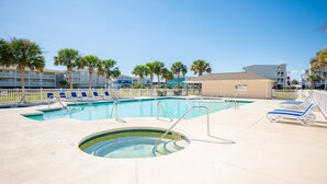 A swimming pool with lounge chairs and palm trees. - Whispering Waves: Ocean View Condo With Covered Balcony (Oak Island)