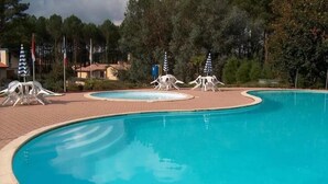 A swimming pool with a curved edge, surrounded by lounge chairs and umbrellas.