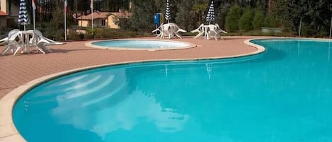 Piscina com borda curva, rodeada por espreguiçadeiras e guarda-sóis.
