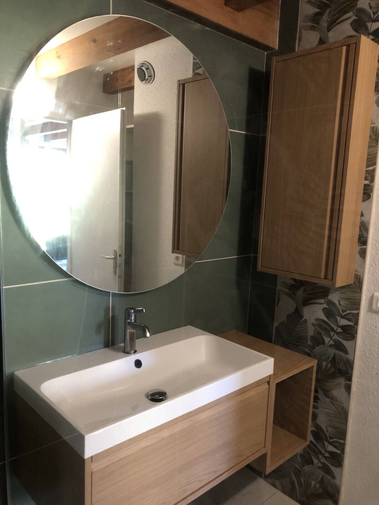 A bathroom with a white sink, a round mirror, and wooden cabinets.