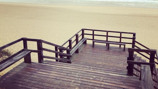 A wooden boardwalk leading to a sandy beach with waves in the background.