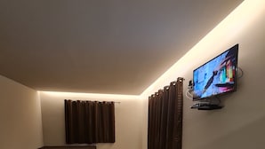 A room with a TV mounted on the wall, a bed, and a seating area with curtains. - Recanto da Pesca Resort (Abaeté)