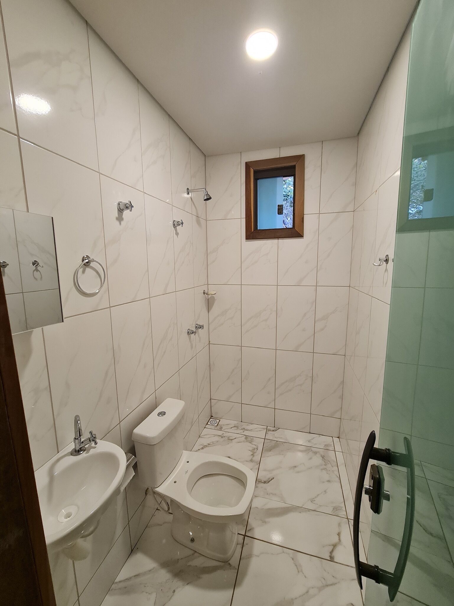 A bathroom with white marble tiles, a toilet, a bidet, a sink, and a shower with a glass door.