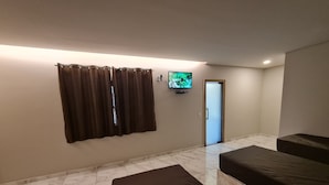 A room with a television mounted on the wall, a door, and two beds with dark covers. - Recanto da Pesca Resort (Abaeté)